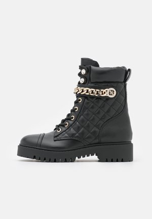 Bottines noires en cuir matelassé avec accent en chaîne dorée, devant à lacets, bout arrondi et semelle en caoutchouc striée. Comprend des boutons décoratifs.