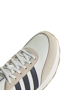 Zapatilla blanca con detalles de ante gris y rayas en azul marino. Presenta un upper de lona texturizada y cordones blancos. Suela gruesa de goma natural.
