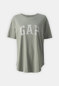 Camiseta de algodón verde oliva con un estampado floral de "GAP" en blanco. Manga corta y un corte relajado con un dobladillo curvado.