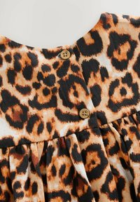 Kangas leopardin kuviolla oranssin, ruskean ja mustan sävyissä; siinä on napitus ja rypytetty rakenne helmaosassa.