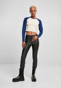 Crop top met een crèmekleurig lichaam en blauwe lange mouwen, gecombineerd met zwarte glanzende leren broeken en zwarte chunky laarzen. Glad textuur overal.