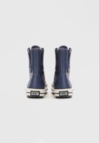 Botas de tobillo de cuero azul con suelas de goma blanca, con un logo All-Star negro y un acabado texturizado. Sin cordones, estilo de poner.