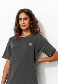 T-shirt gris foncé en tissu doux, avec des manches retroussées et une broderie en forme de cœur à imprimé léopard sur la poitrine.