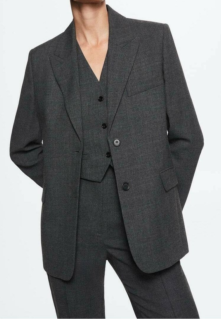 Costume gris foncé sur mesure avec gilet et pantalon assortis porté par une personne les mains derrière le dos, visible du cou jusqu'à mi-cuisse sur fond blanc.