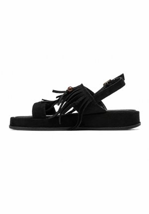 Sandale en daim noir avec semelle plateforme plate, détails à franges sur le dessus, une perle en bois et une bride de cheville réglable avec boucle.