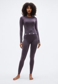 Μωβ εφαρμοστό τοπ με μακριά μανίκια και κολάν από μαλακό, ελαστικό υλικό με υφή. Διακοσμητικό σχέδιο στη μέση.