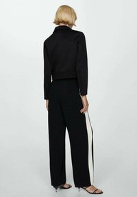 Czarna krótka kurtka z kołnierzykiem, z teksturowanej tkaniny; zestawiona z szerokimi czarnymi spodniami, które mają biały pasek po boku.