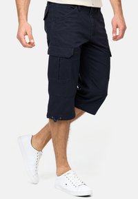 Navy cargo shorts made of cotton with multiple pockets, a relaxed fit, and drawstring detail at the hem, paired with white sneakers.
