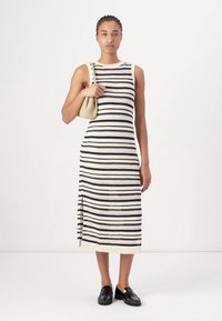 Robe sans manches en tricot avec des rayures horizontales bleu marine et blanches, dotée de fentes latérales et d'une texture douce. Associée à un petit sac à main léger.