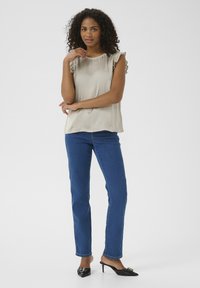 Un haut beige clair avec des manches courtes à volants, associé à un jean bleu droit et des mules à talons noirs avec des accents décoratifs.
