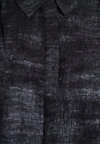 Black denim fabric close-up showing a shirt collar and front seam with a faded, textured wash effect.