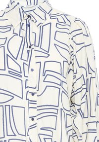 Camicia bianca con un motivo geometrico blu, colletto strutturato e chiusura con bottoni, maniche lunghe e tessuto testurizzato.