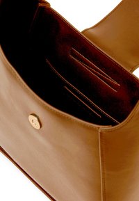 Brown leather handbag with a smooth texture, featuring a round gold button closure, and interior pockets for organization.