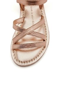 Sandalias en oro rosado con correas de cuero metálico que se cruzan sobre una suela plana, con costuras detalladas a lo largo del borde.