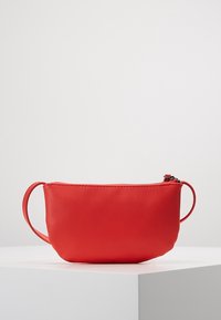 Červená kožená taška s jemnou texturou, zaobleným tvarem a zipovým uzávěrem. Má jeden držák na jedné straně pro snadné nošení.