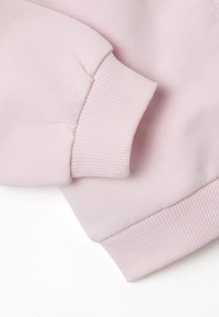 Polsino di felpa rosa chiaro con texture a coste e finitura liscia. Il tessuto è morbido, offrendo comfort e flessibilità.