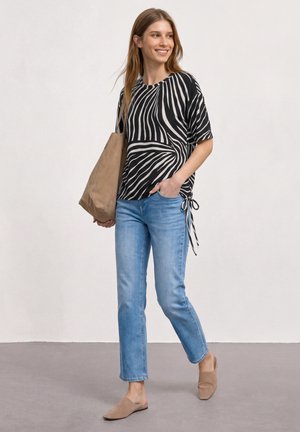 Femme marchant portant un haut à manches courtes rayé noir et blanc, un jean bleu clair, des chaussures beiges sans lacets et un grand sac cabas beige.