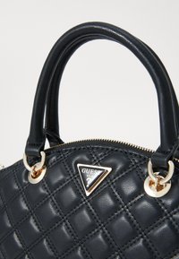 Borsa a tracolla in pelle nera trapuntata con doppi manici, hardware dorato e logo a forma triangolare. Superficie testurizzata e chiusura con zip.