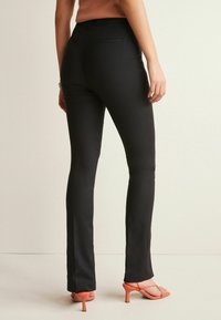 Zwarte pantalon met slim fit, subtiel gestructureerde stof, middelhoge taille en achterzakken; gecombineerd met pasteloranje hoge hakken.