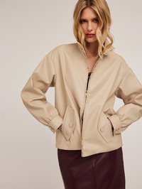 Giacca in finta pelle beige con collo alto, chiusura con zip e polsini elasticizzati. Presenta tasche a toppa oblique e una texture liscia.