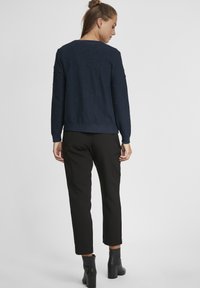 Pull en tricot navy avec un motif texturé en boucles, col rond et ourlet en côtes, associé à un pantalon noir fuselé et des bottines.