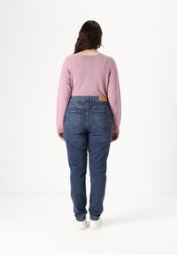 Light pink sweater with long sleeves paired with blue denim jeans. Soft texture and fitted design. White sneakers complete the outfit.