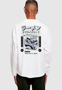 Balta ilgomis rankovėmis marškiniai su juodu grafiniu dizainu ant nugaros, vaizduojančiu ramen makaronus ir tekstą japonų kalba, su tinklo fono.