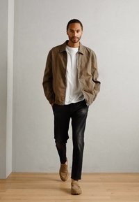 Jachetă bombă bej deschis peste un tricou alb, asortată cu blugi negri și mocasini bej. Țesătură fină, croială relaxată, design minimalist.