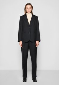 Svart pinstripe dress med en strukturert blazer som har notched lapels, to frontlommer og matchende skreddersydde bukser. Teksturert stoff.
