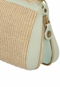 Bolso tejido color tostado con ribete de cuero verde menta y cremallera dorada. Presenta una superficie texturizada y un bolsillo redondeado con cremallera.