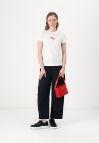 Bílý tričko s červeným logem, tmavě modré široké kalhoty, černé tenisky a malá červená kabelka se zlatými doplňky. Jednoduchý neformální outfit.