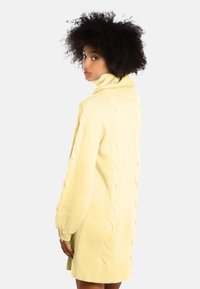 Abito maglione giallo a maglia con collo alto, maniche lunghe, motivo testurizzato e bottoni ai polsini. Materiale morbido, vestibilità comoda.