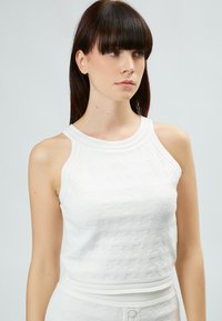 Top bianco senza maniche con motivo in maglia strutturata, caratterizzato da un collo rotondo a coste e spalline. Design aderente senza hardware visibile.