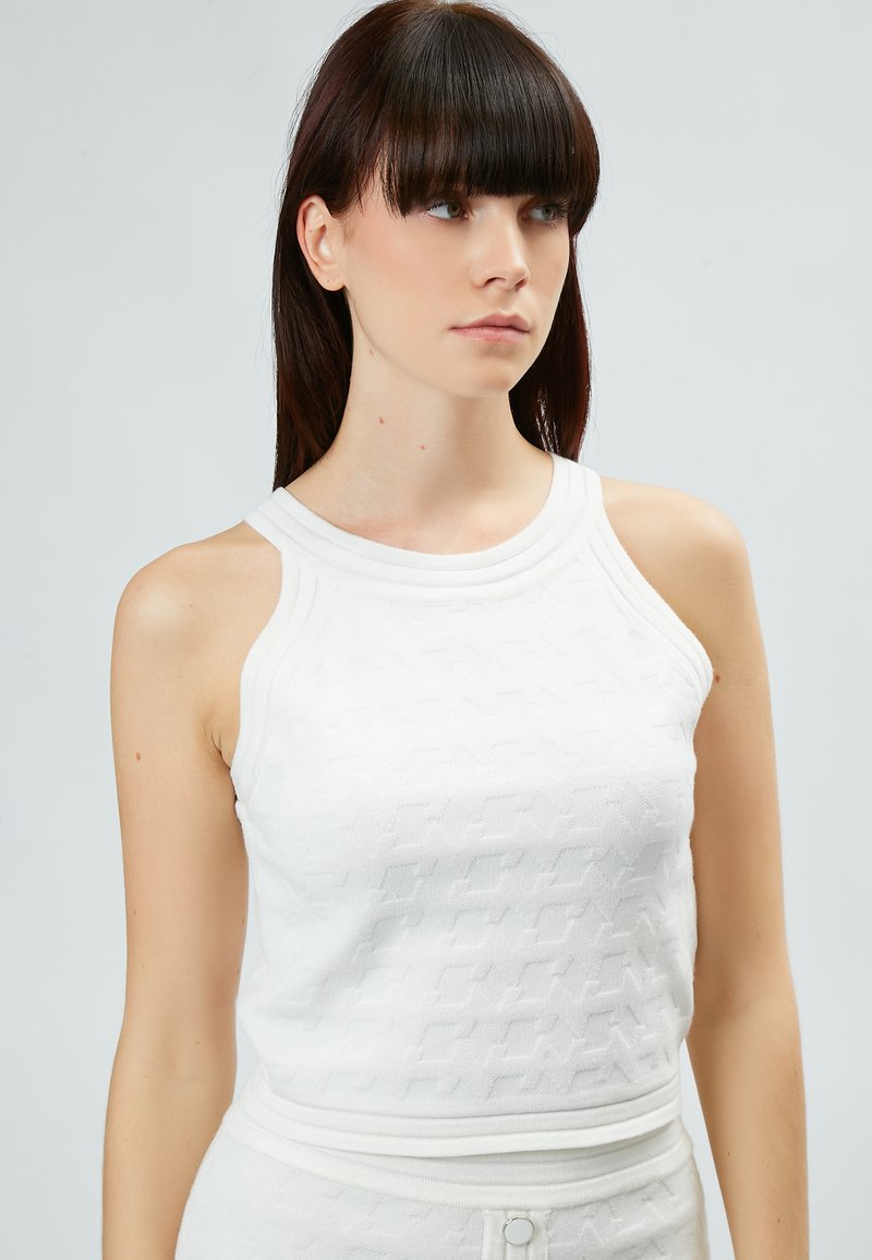 Top bianco senza maniche con motivo in maglia strutturata, caratterizzato da un collo rotondo a coste e spalline. Design aderente senza hardware visibile.