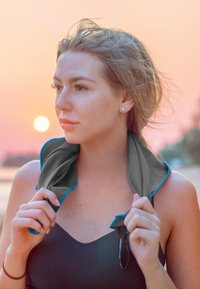 Cooling towel with gray body and blue trim. Worn around the neck, fabric appears smooth and lightweight. Background features a sunset.