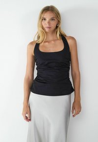 Top in tessuto nero arricciato con scollatura quadrata e spalline larghe, abbinato a una gonna in satin argento. Texture liscia e design aderente.