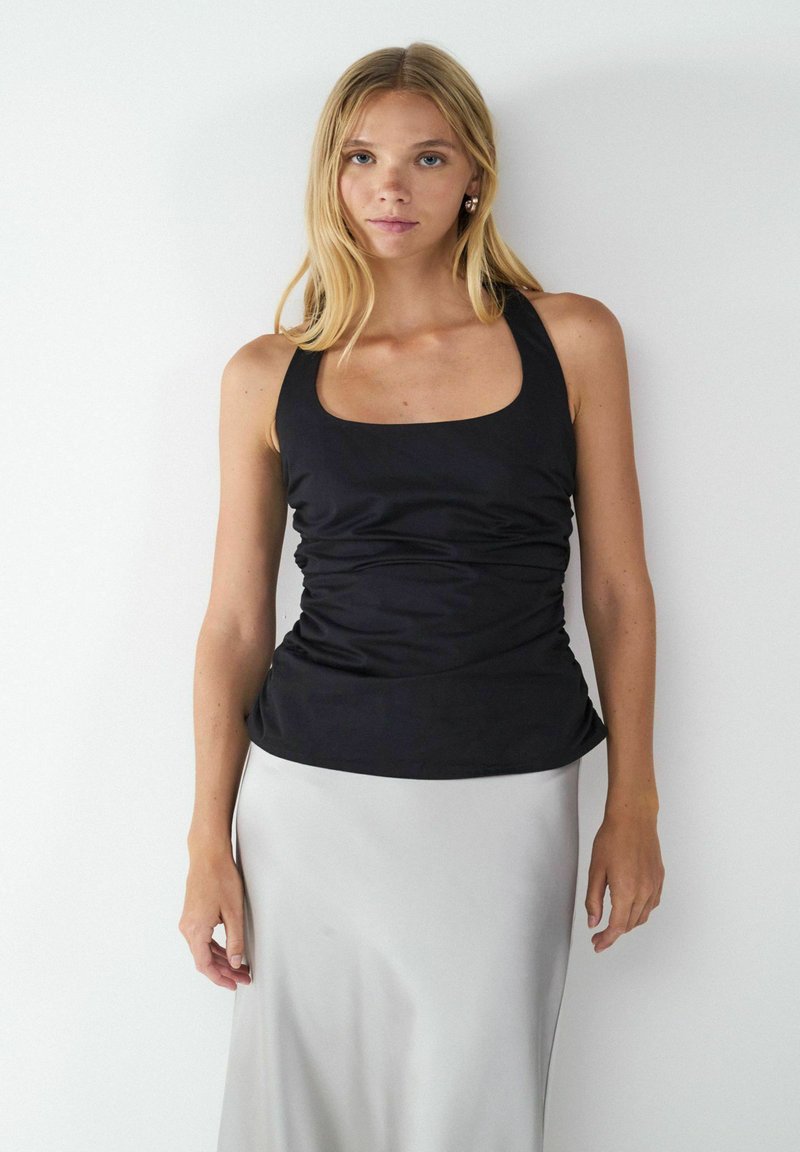 Top in tessuto nero arricciato con scollatura quadrata e spalline larghe, abbinato a una gonna in satin argento. Texture liscia e design aderente.