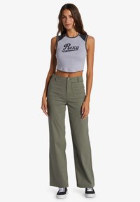Grijze cropped tanktop met zwarte accenten en het "Roxy"-logo, gecombineerd met olijfgroene wijde broek en zwarte sneakers.