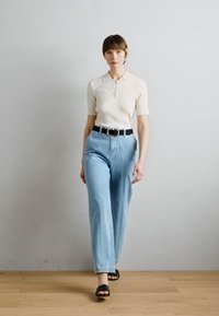 Polo shirt beige a coste con maniche corte, jeans azzurri a vita alta, cintura nera con fibbia circolare e sandali neri.