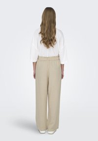 Bøyd hvit bluse med løse ermer, parret med vide beige bukser med strukturert stoff og elastisk midje.
