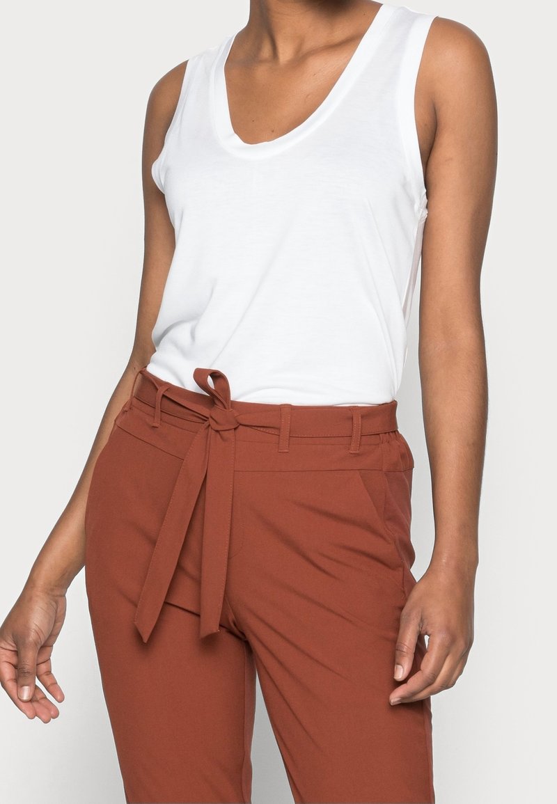 Top bianco senza maniche abbinato a pantaloni a vita alta color ruggine con cintura annodata. Tessuto morbido con una vestibilità comoda e design minimal.