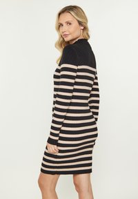 Gestreiftes Kleid mit schwarzen und hellbeigen horizontalen Streifen, langen Ärmeln und hohem Ausschnitt, entworfen für eine figurbetonte Silhouette.