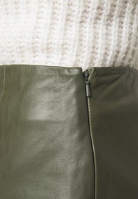 Oliivinvihreä nahkahame, jossa on sileä pinta ja sivuvetoketjukiinnitys. Se on yhdistetty kermaiseen neulepaitaan.