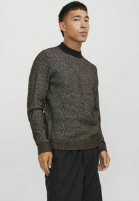 Suéter de punto en marrón oscuro con un acabado texturizado. Cuenta con un cuello redondo acanalado negro y puños, y una silueta ajustada.