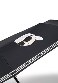 Parapluie noir arborant un design graphique d'un visage avec des lunettes de soleil. Mis en valeur par une bande de logo blanche sur le bord. Texture de tissu lisse.