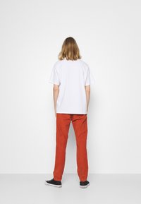 T-shirt blanc à manches courtes associé à un pantalon en velours côtelé orange et des baskets noires. Le vêtement a une coupe décontractée avec une texture lisse.