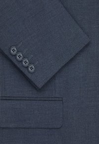 Granatowa marynarka z teksturowanej tkaniny, z klapami i czterema czarnymi guzikami na mankiecie. Zawiera kieszeń na piersi.