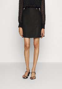 Minifalda negra texturizada con forma ajustada, con un detalle de botones laterales. Combinada con sandalias de tacón negras con tiras.