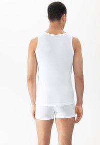 Witte tanktop en shorts, gemaakt van ademend materiaal. De tanktop heeft brede banden en een zachte textuur; de shorts zijn aangesloten met een contrasterende tailleband.