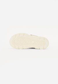 Skosåle med teksturert overflate, med et mønstret dekkdesign. Fargen er lys beige med hevede detaljer for grep og holdbarhet.